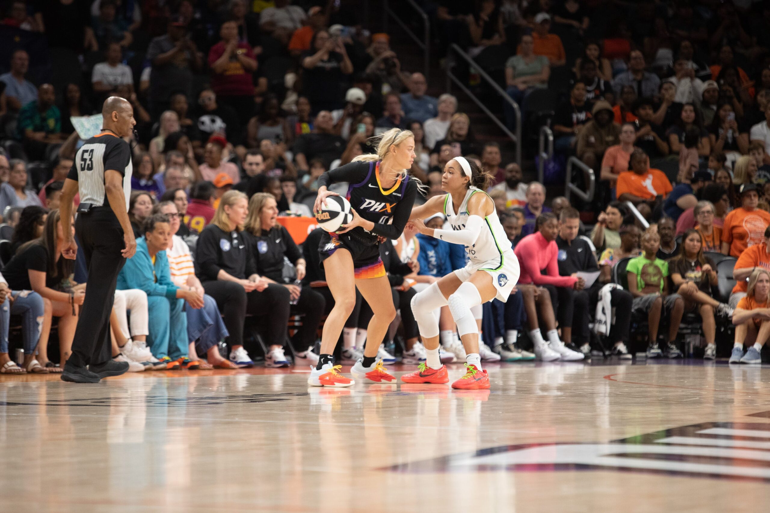Phoenix Mercury guard Sophie Cunningham holds the ball on her right side on the perimeter. Minnesota Lynx forward Napheesa Collier is in a defensive stance and guarding her tightly.