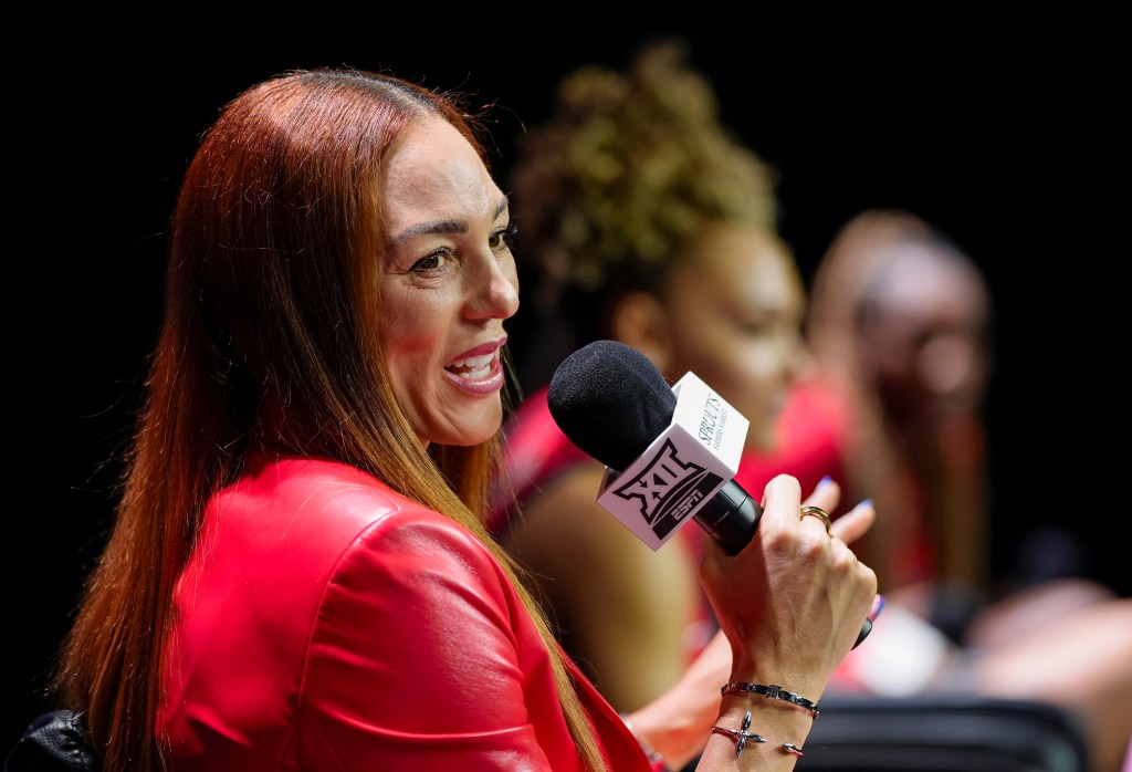Arizona head coach Adia Barnes is shown in profile, speaking into a handheld microphone that has the Big 12 and ESPN logos on it.