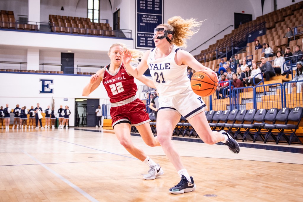 Yale guard Kiley Capstraw dribbles with her left hand near the baseline. Her eyes are up, toward the rim, and she wears a clear protective face mask.