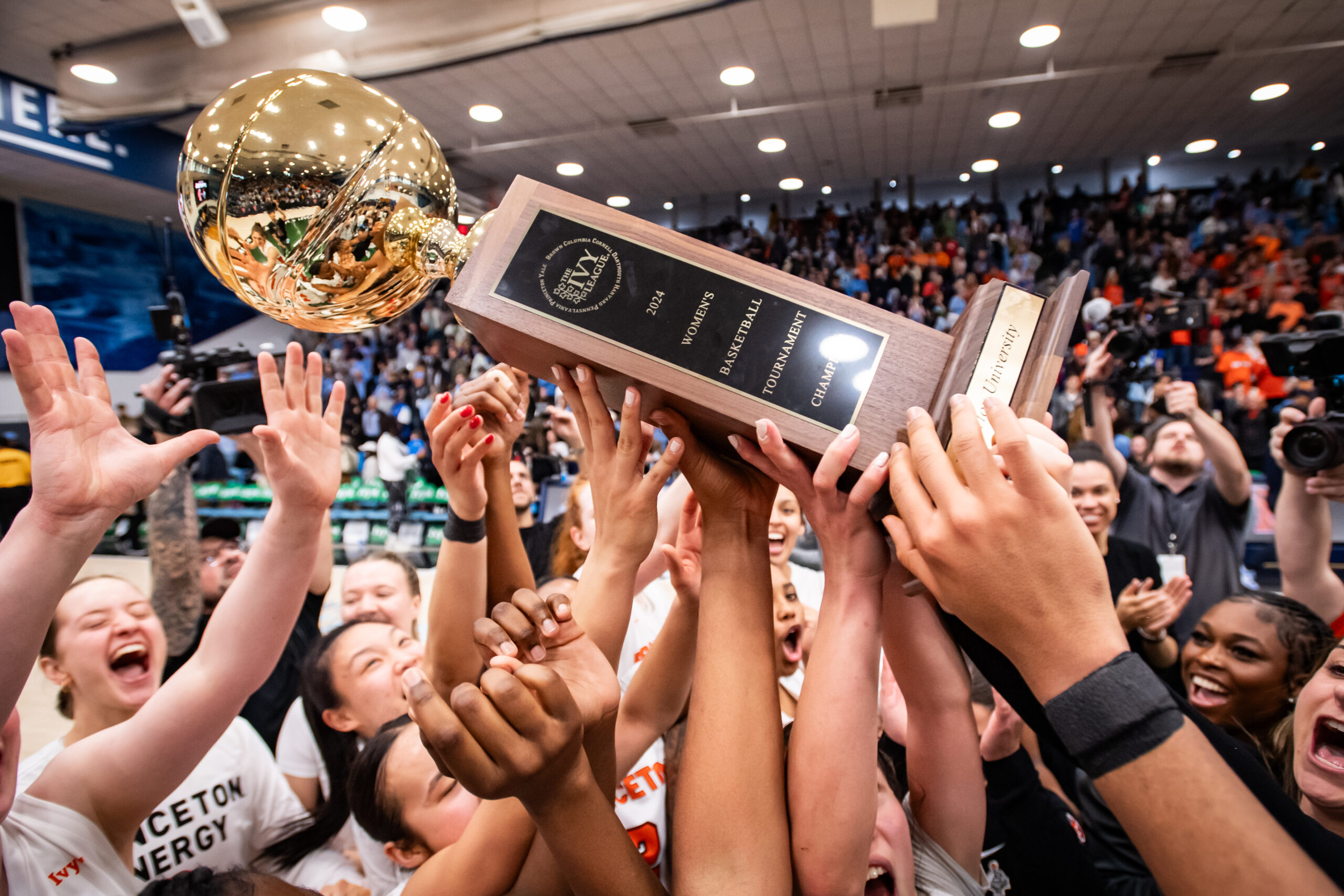 Princeton players hold the Ivy League Tournament championship trophy aloft. It is a gold ball on top of a long wooden base.