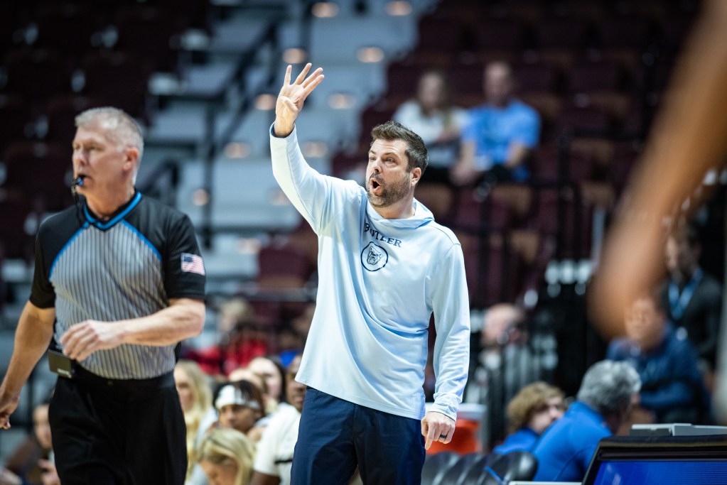 Butler coach Austin Parkinson stands on the sideline with right hand raised holding up four fingers
BIG EAST