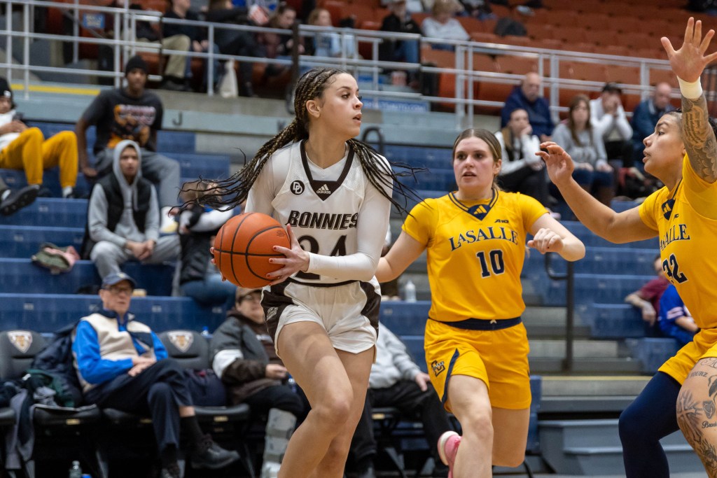 Payton Fields holds the ball to her right as she looks for an open teammate as a defender stands in front of her and a second defender comes from her left side.