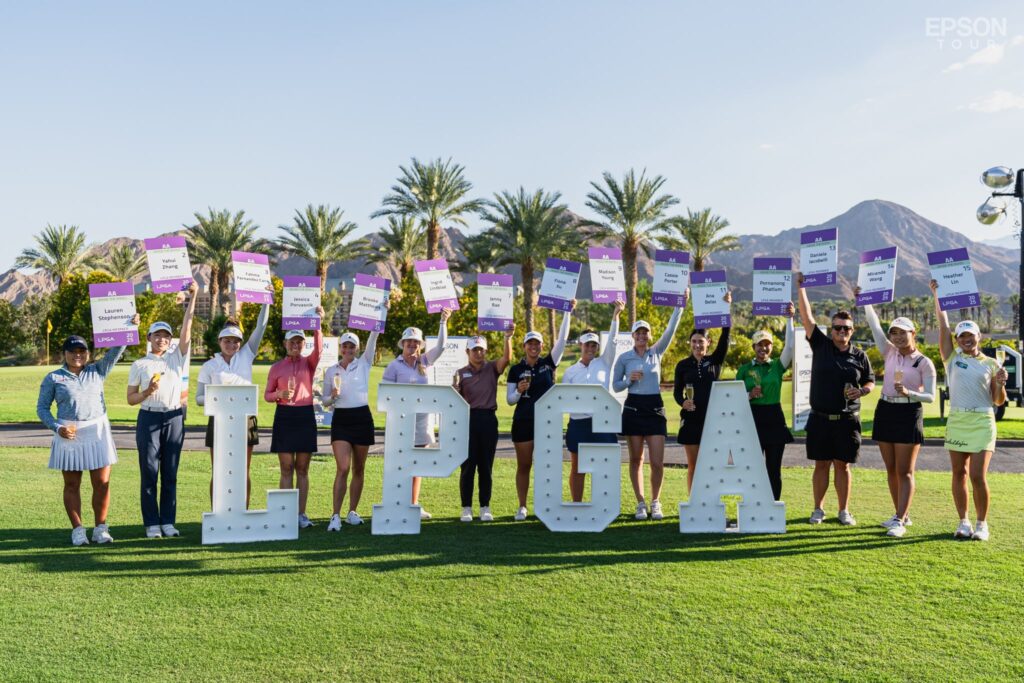 15 Epson Tour graduate golfers pose behind large block letters spelling "LPGA" and hold up signs with each of their names