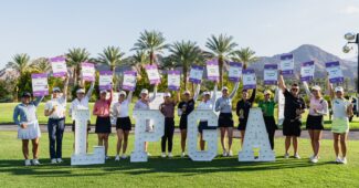 15 Epson Tour graduate golfers pose behind large block letters spelling "LPGA" and hold up signs with each of their names