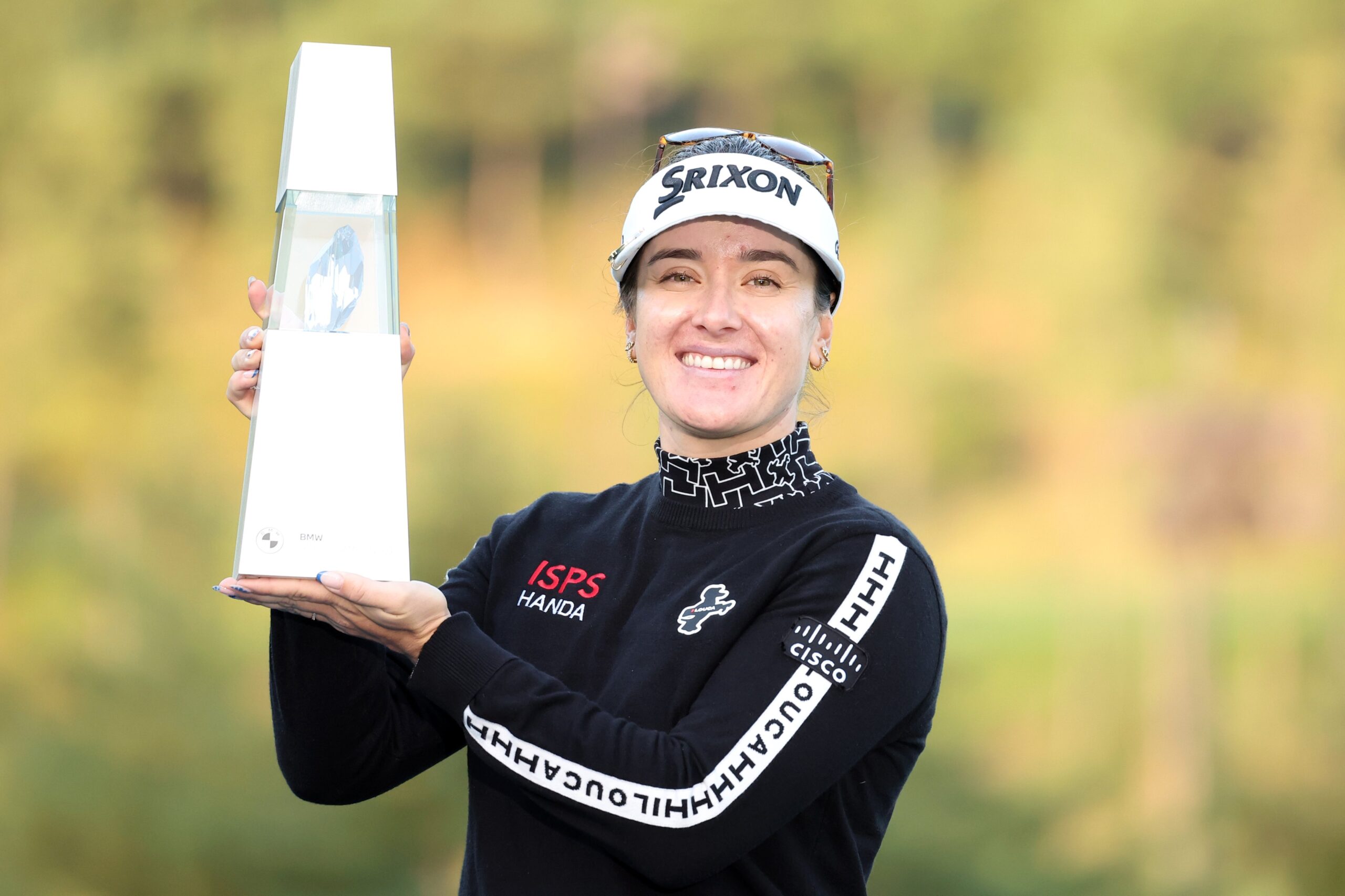 Hannah Green smiles and holds up the BMW Ladies Championship trophy to her right.