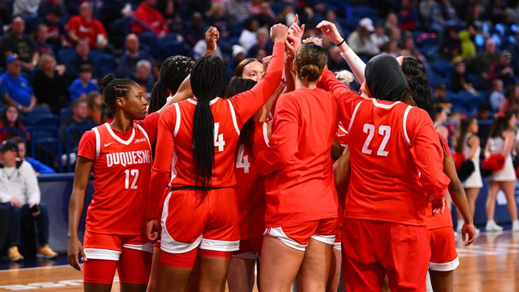 Duquesne players raise their hands towards the center of the huddle.