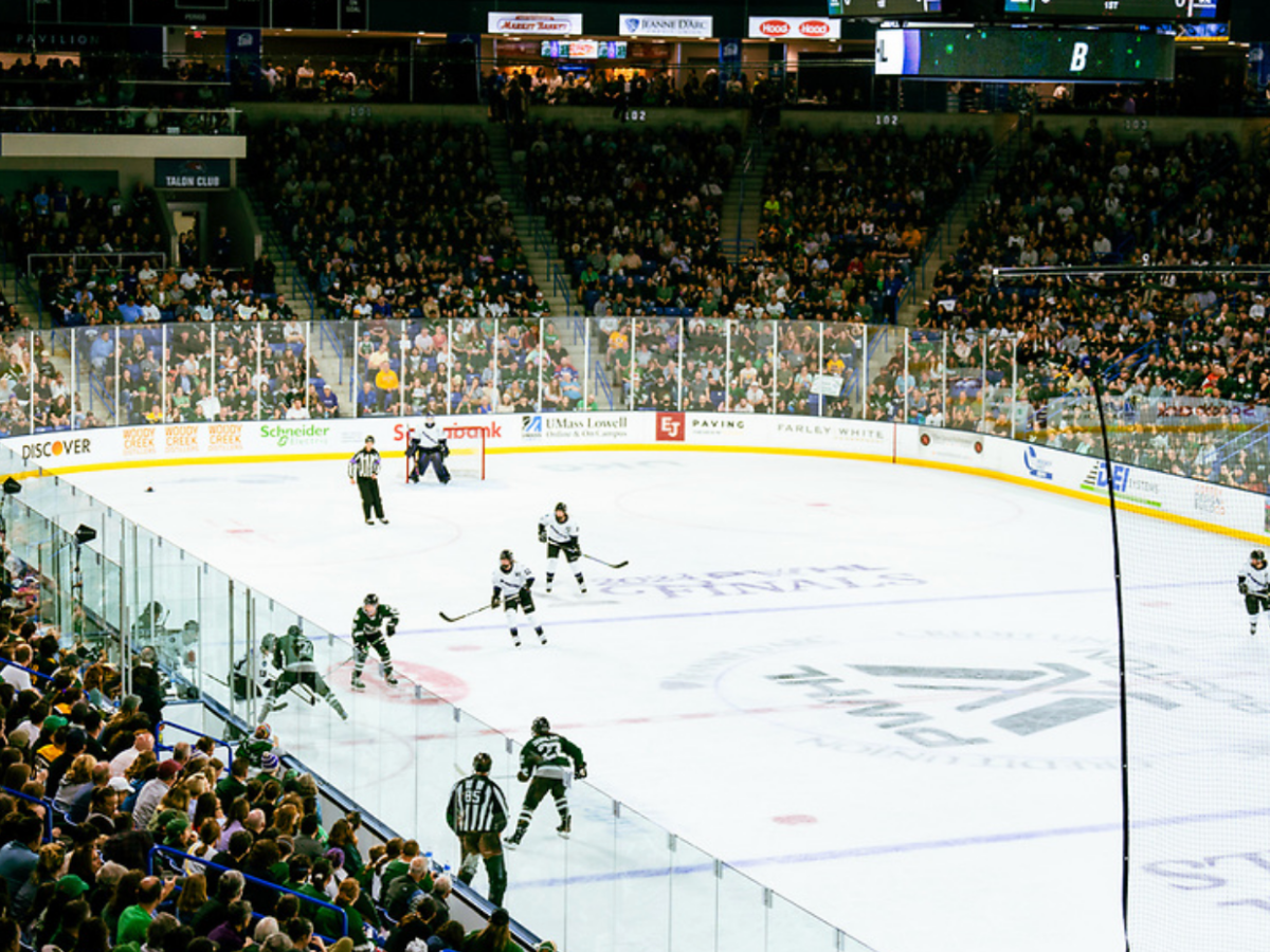 An above-ice level shot of Boston and Minnesota playing. There is an ongoing battle near the boards for the puck.
