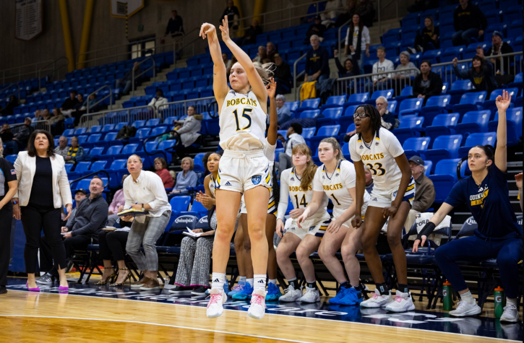 Quinnipiac guard Karson Martin shoots an open 3-pointer in front of the Bobcats' bench. Many of the players on the bench start to stands up in anticipation.