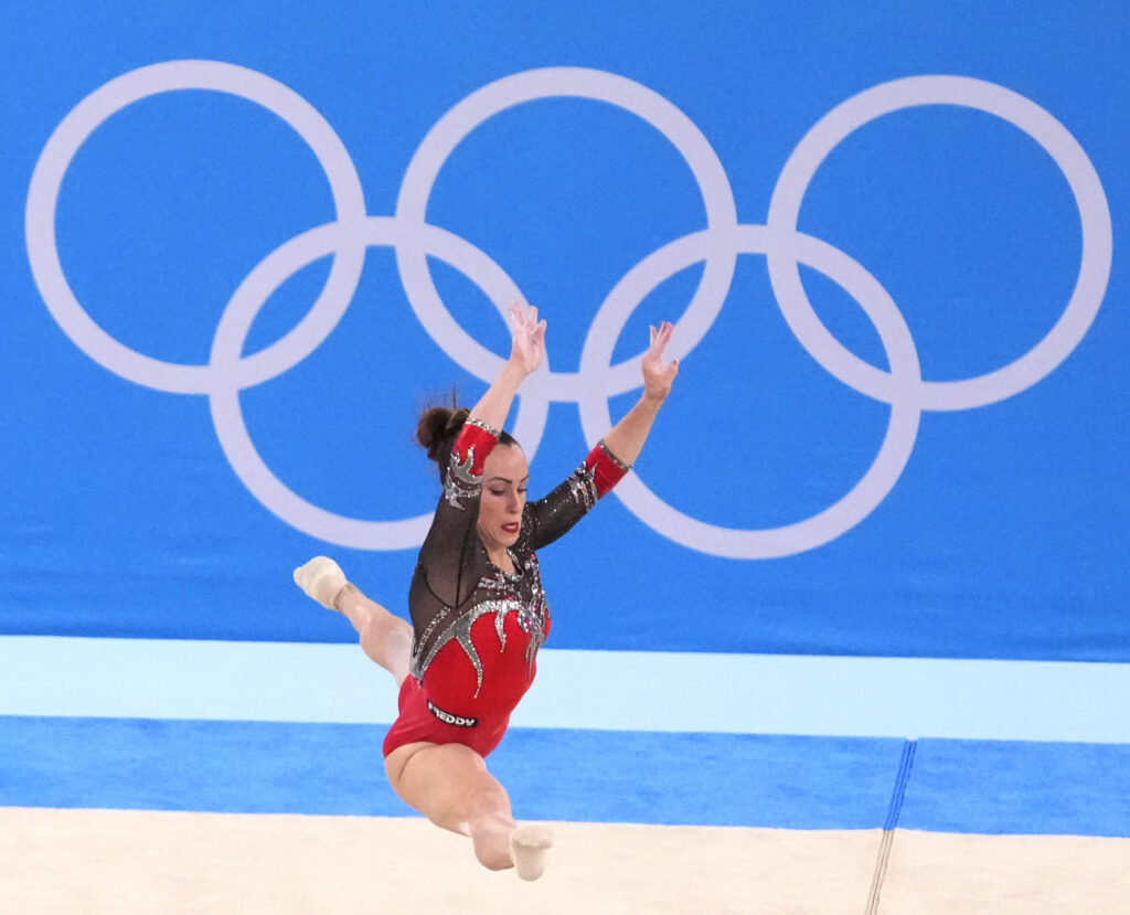 Gymnast in a red leotard competes a leap on floor at the Tokyo Olympics in 2021.