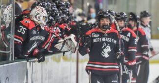 Northeastern hockey team high-fives teammates on the bench while skating on the ice