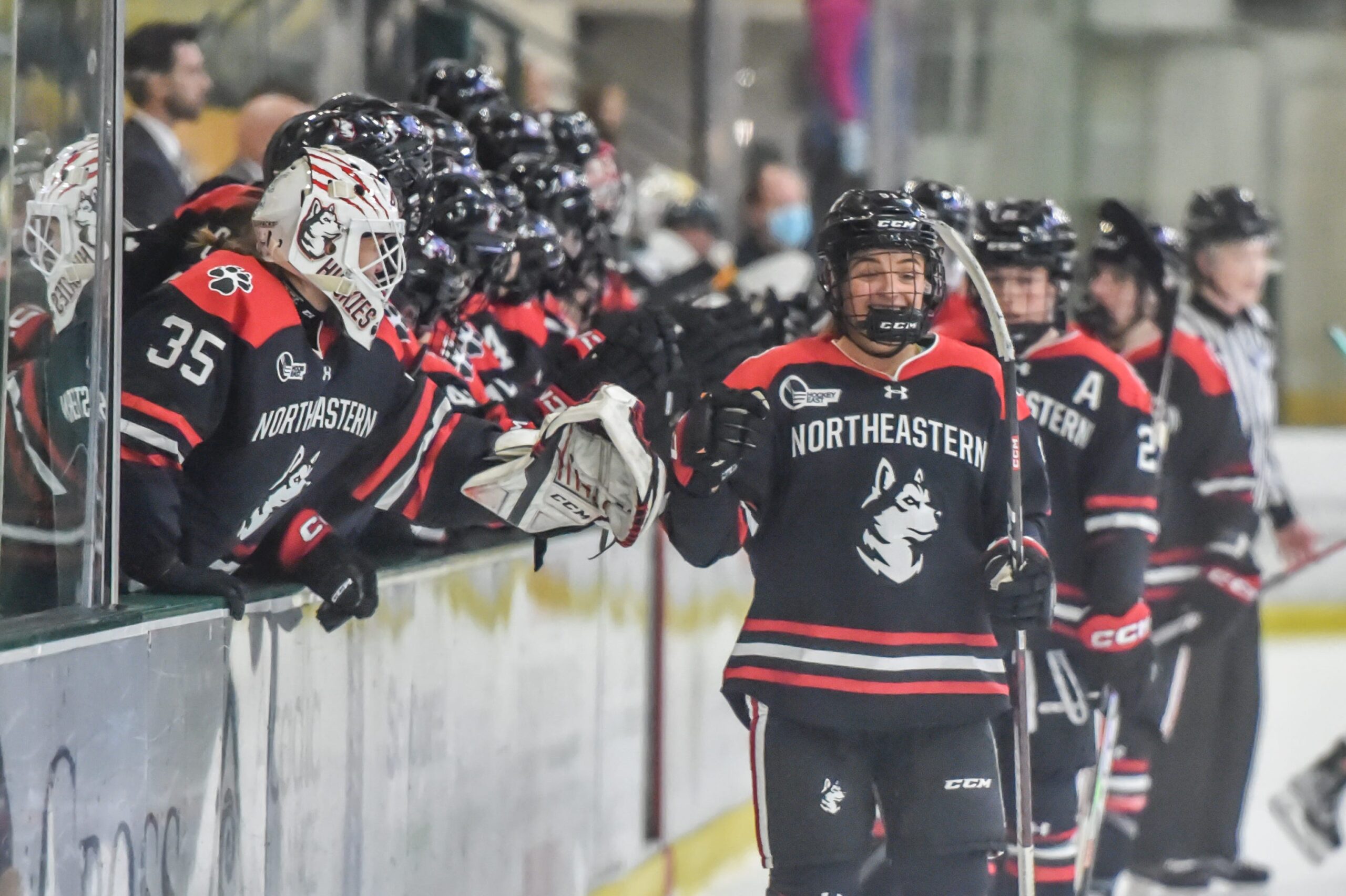 Northeastern hockey team high-fives teammates on the bench while skating on the ice