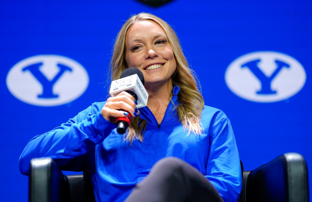BYU head coach Amber Whiting smiles as she holds a microphone and takes questions during Big 12 media days.