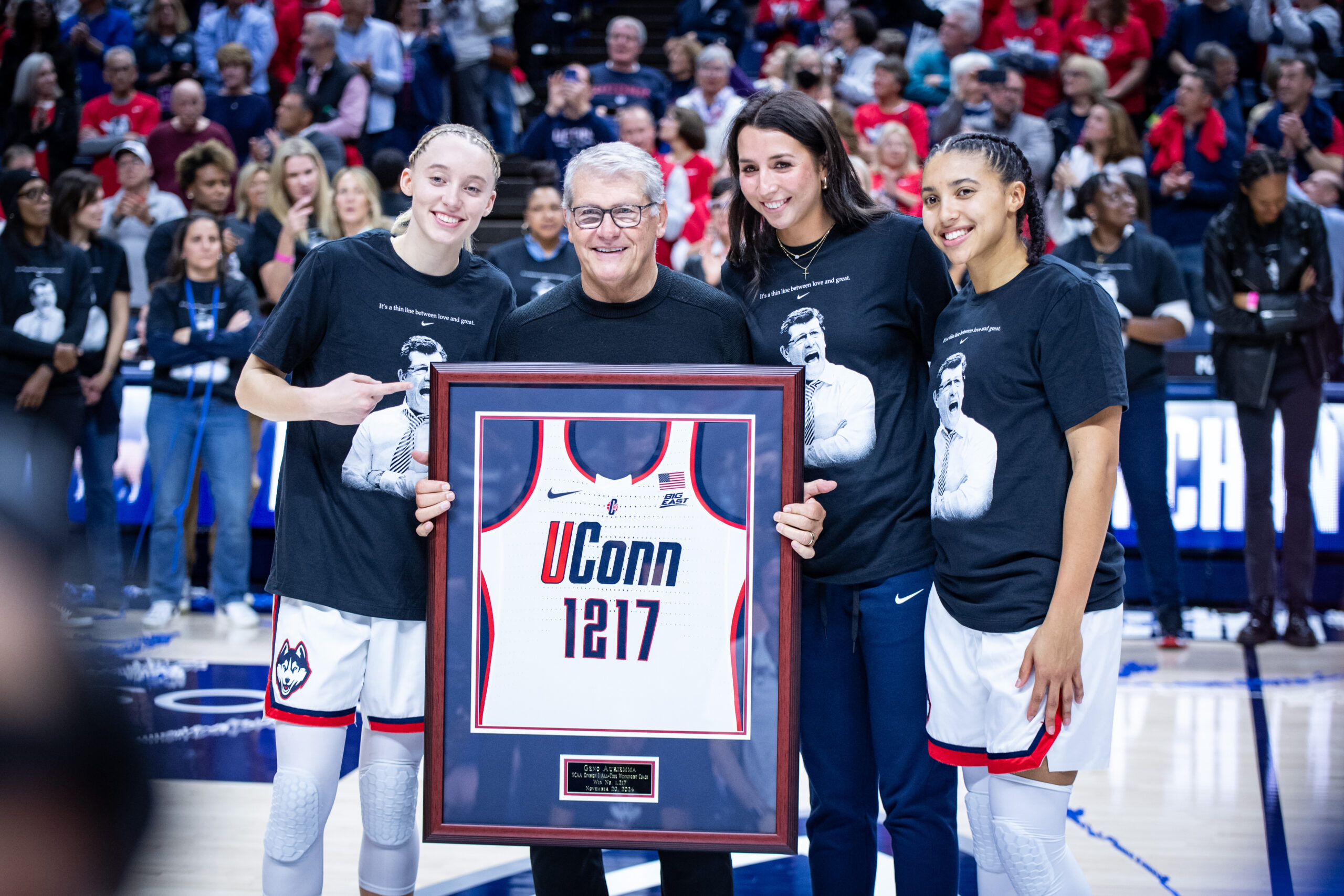 UConn players and head coach Geno Auriemma pose with a frame UConn jersey with the number 1,217