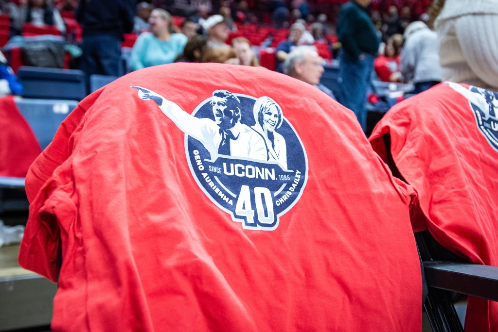 A ruby red t-shirt featuring Geno Auriemma and Chris Dailey is draped over a seat at Gampel Pavilion.