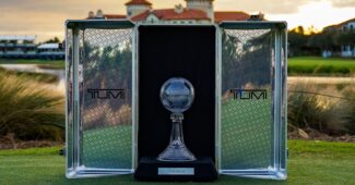 The CME Group Tour Championship trophy sits in a case between two crystal cases. The sun sets on a golf course as a backdrop for the photo.
