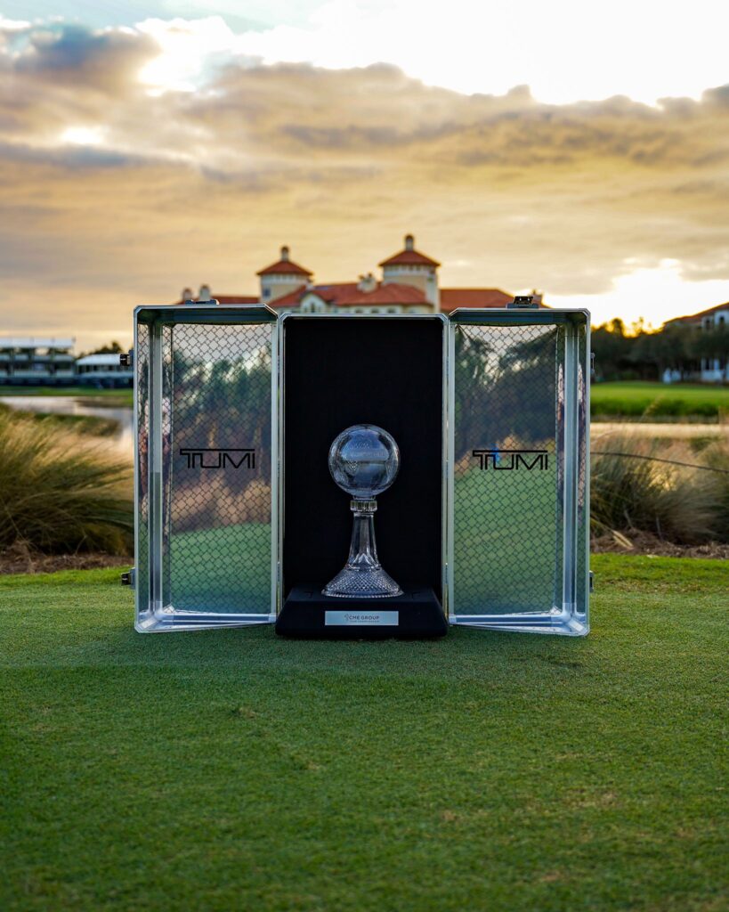 The CME Group Tour Championship trophy sits in a case between two crystal cases. The sun sets on a golf course as a backdrop for the photo.