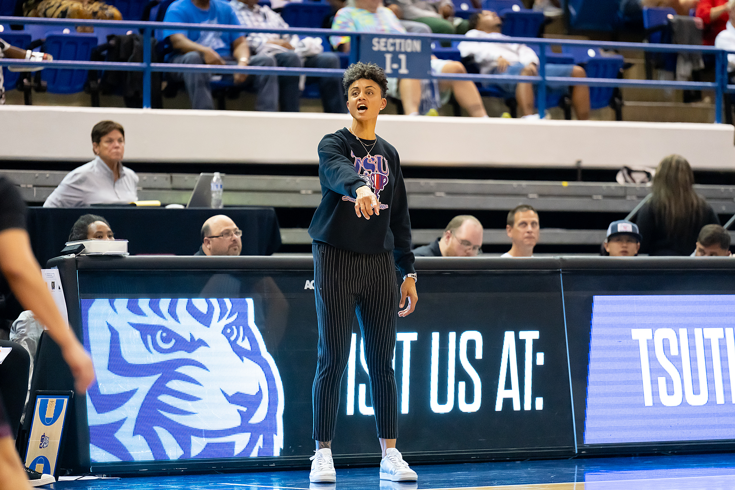 Candice Dupree stands on the Tennessee State sideline, points in front of her and says something to someone outside the frame.
