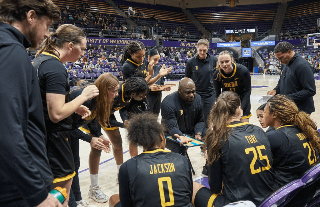 Siena head coach Terry Primm (middle) guides his team around him using a clipboard 