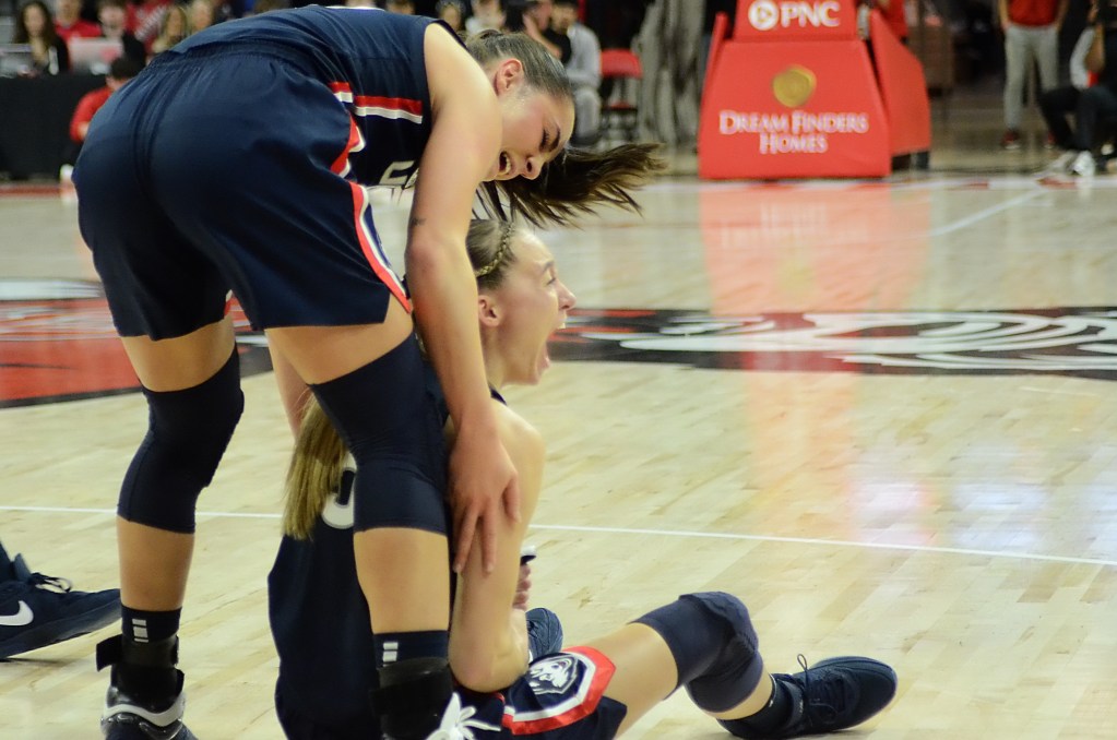 UConn guard Nika Muhl stands over UConn guard Paige Bueckers, who sits on the floor. The two are celebrating after a play during a game.