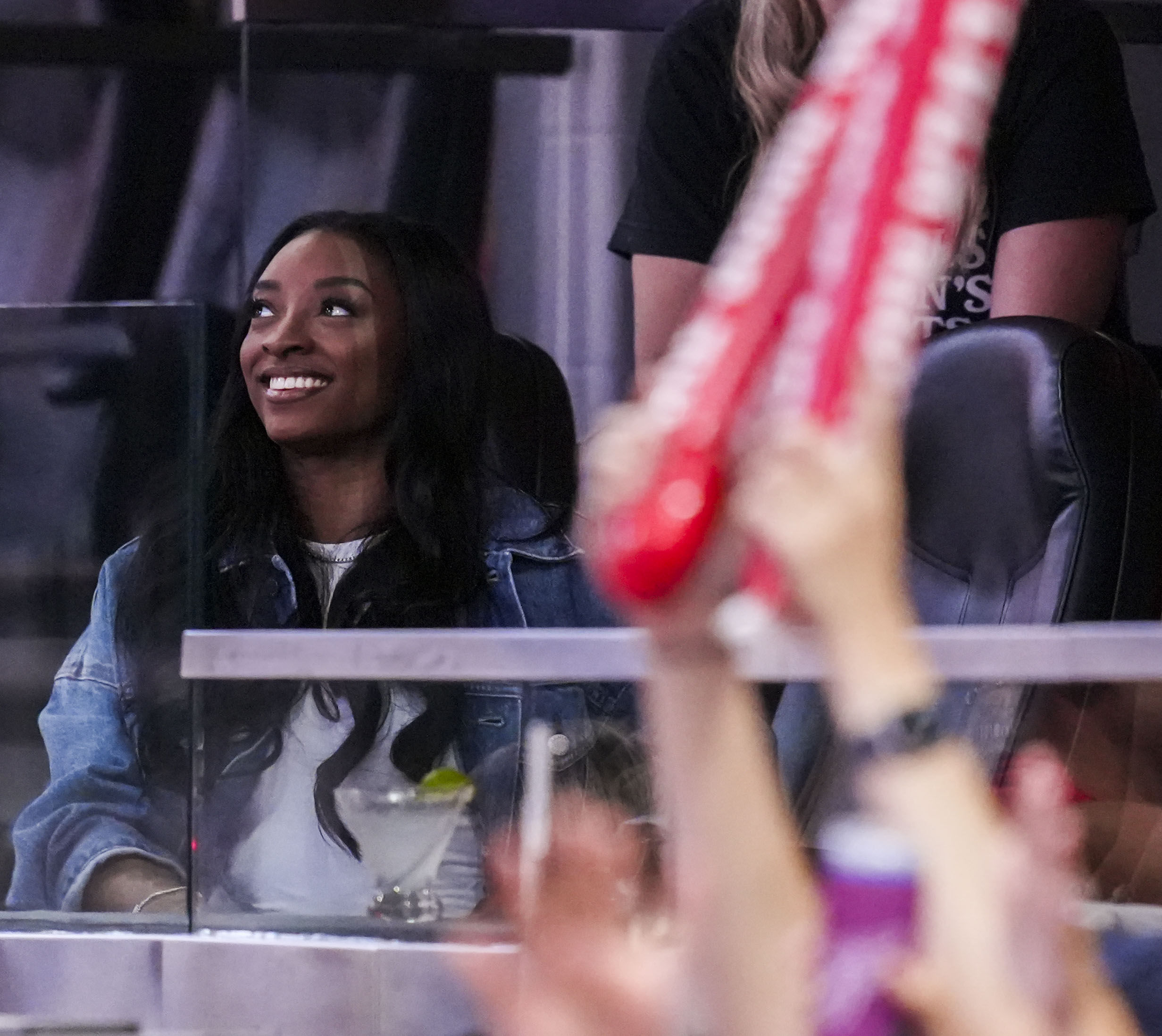 Simone Biles in the stands at an NBA game, looking off to the right.