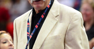 Gymnastics coach Bela Karolyi, in a tan sports coat, watches a competition.