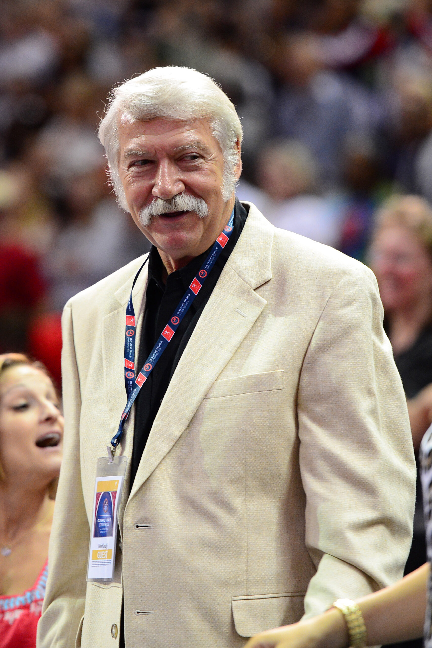 Gymnastics coach Bela Karolyi, in a tan sports coat, watches a competition.