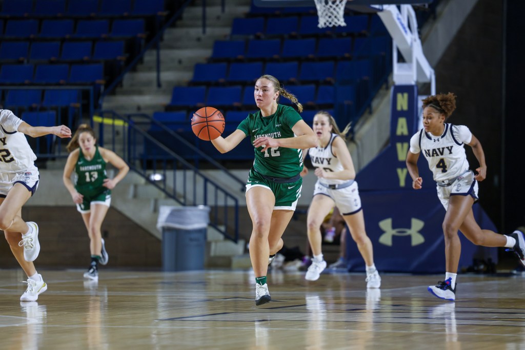 Dartmouth forward Olivia Austin dribbles the ball with her right hand in transition. Two Navy players are visible behind her, trying to catch up.