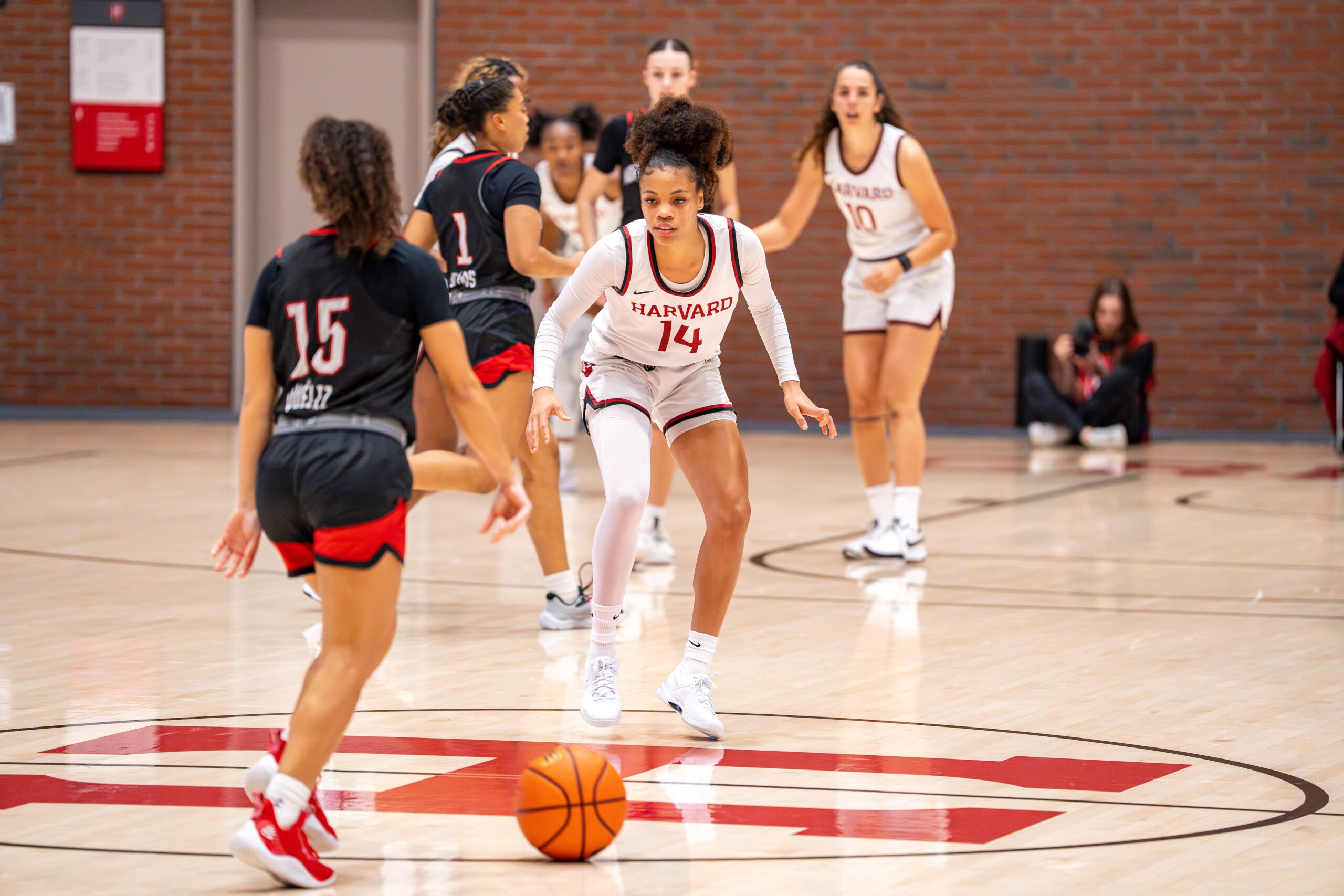 Harvard guard Harmoni Turner stands in a defensive stance inside the halfcourt circle, ready to defend a Northeastern player when she crosses halfcourt with the ball.