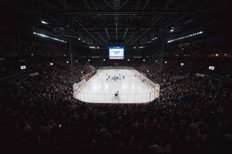 A wide-angle shot of the ice from behind Desbiens' net. The ice appears far away and the packed stands are also visible.