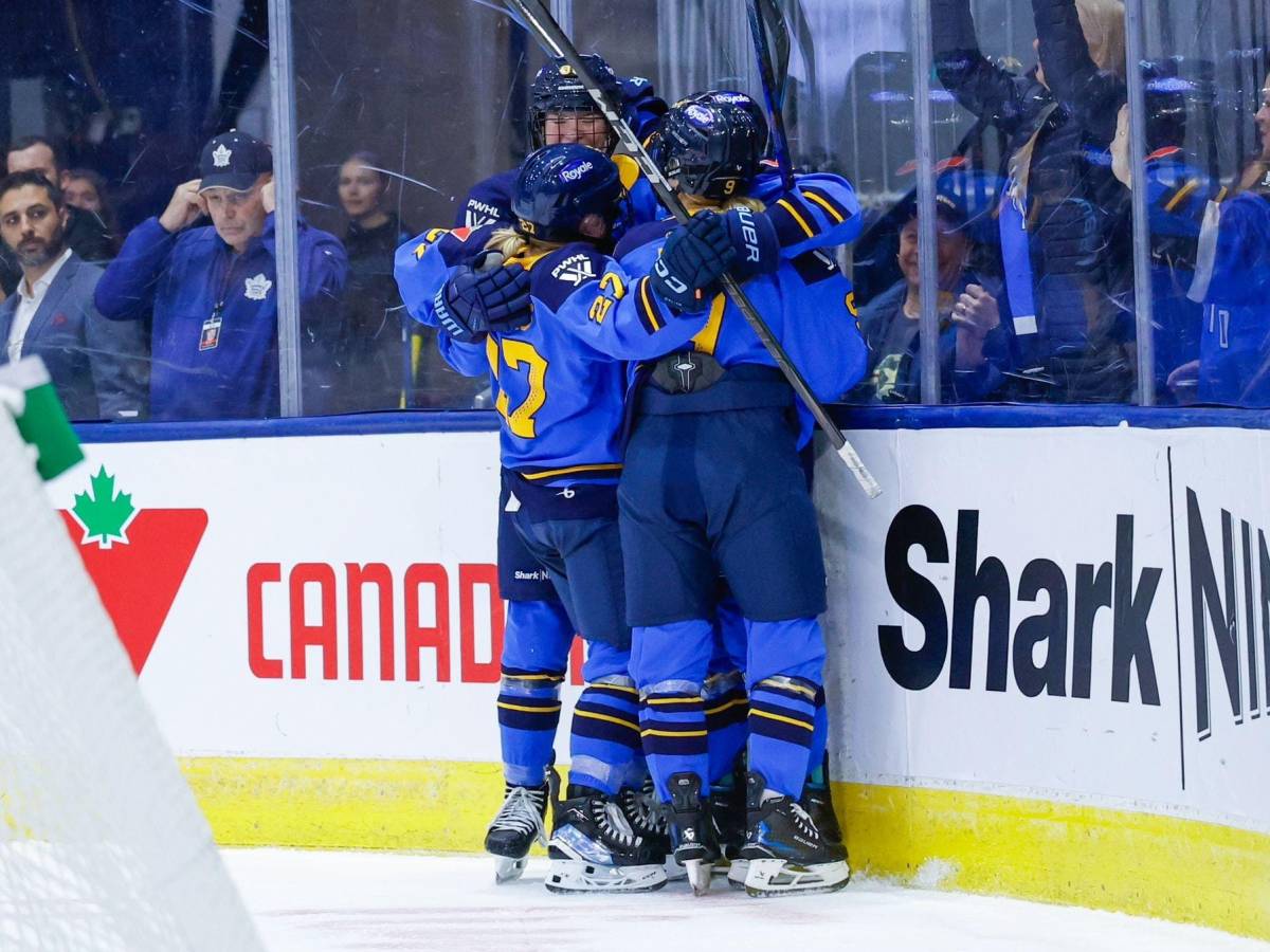 Sceptres players celebrate a goal with a tight group hug behind the net. They are wearing blue home uniforms.