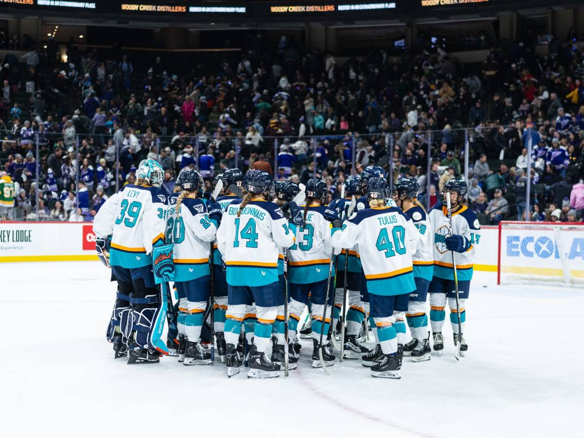 A from-behind look at the entire Sirens team in a tight huddle. They are wearing white away jerseys.