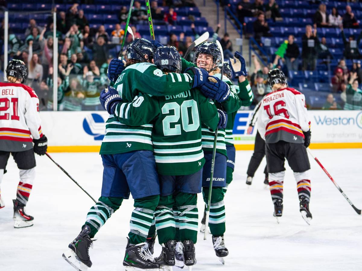Fleet players celebrate a goal with a tight group hug. They are all wearing green home uniforms.