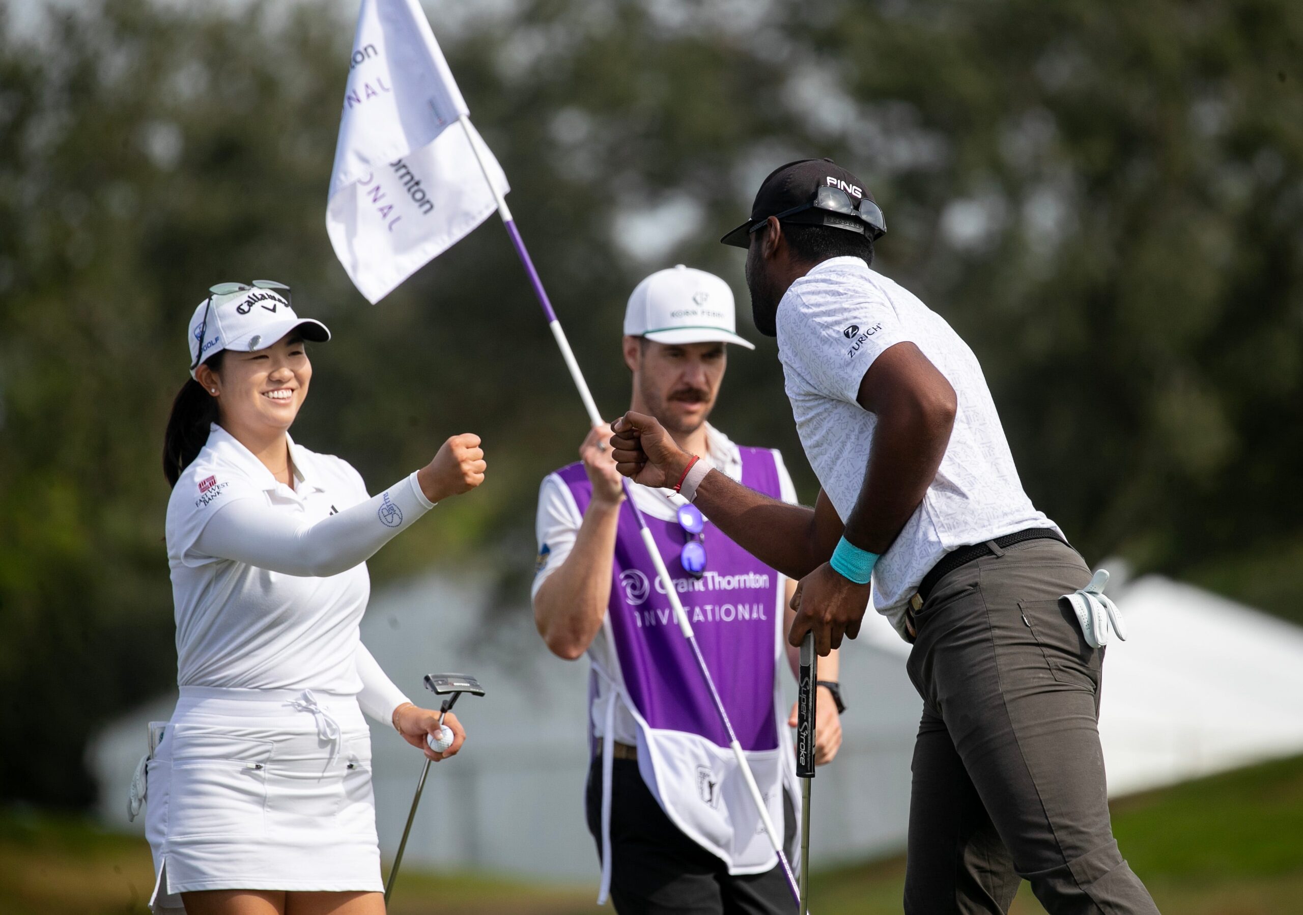 Rose Zhang extends a fist to celebrate with Sahith Theegala. A caddie holds the flag in the background.