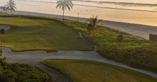 A golf course from an aerial view with the ocean and a sunset in the background