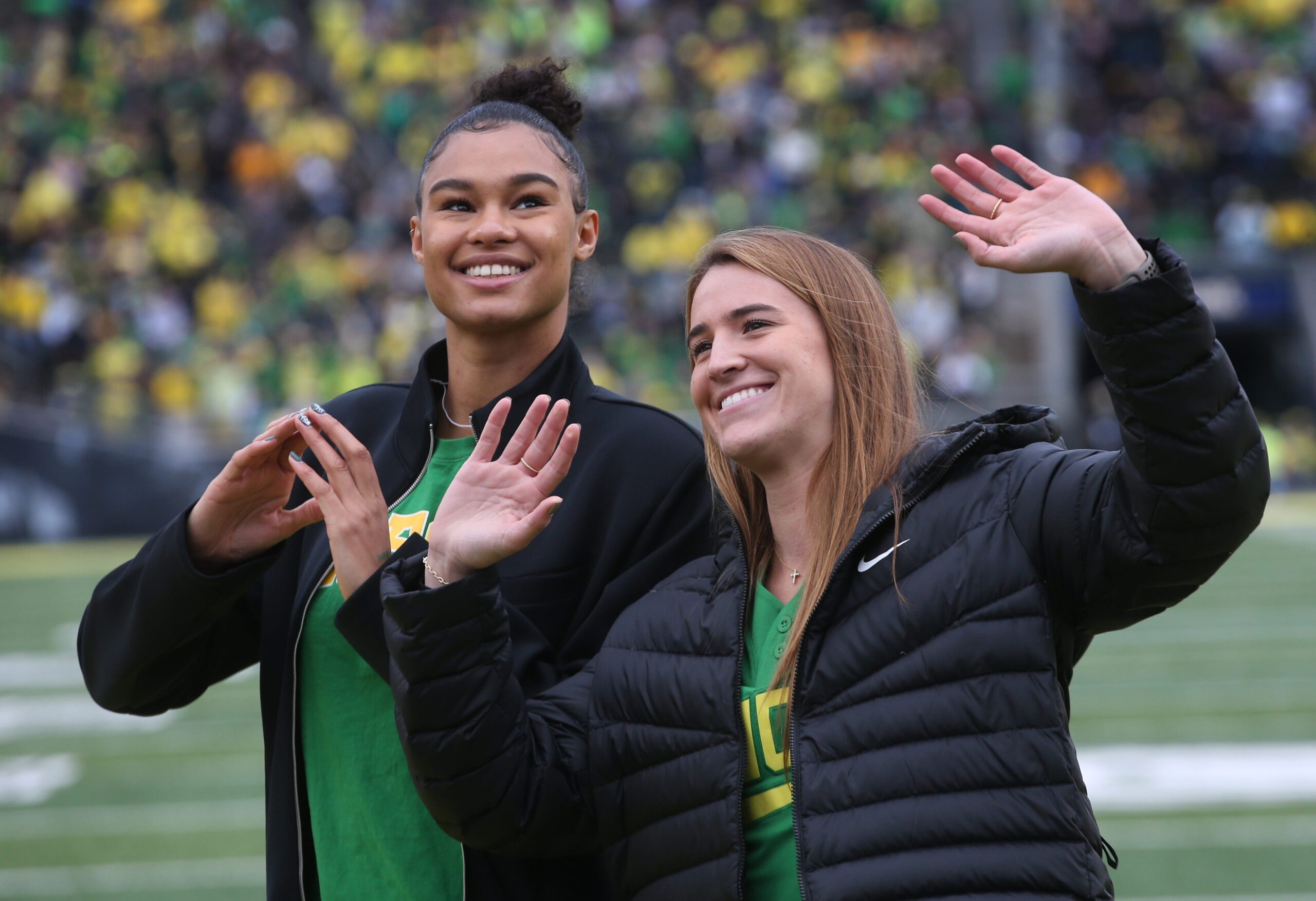 Former Oregon women's basketball stars Sabrina Ionescu and Satou Sabally wave to the crowd at an Oregon football game.