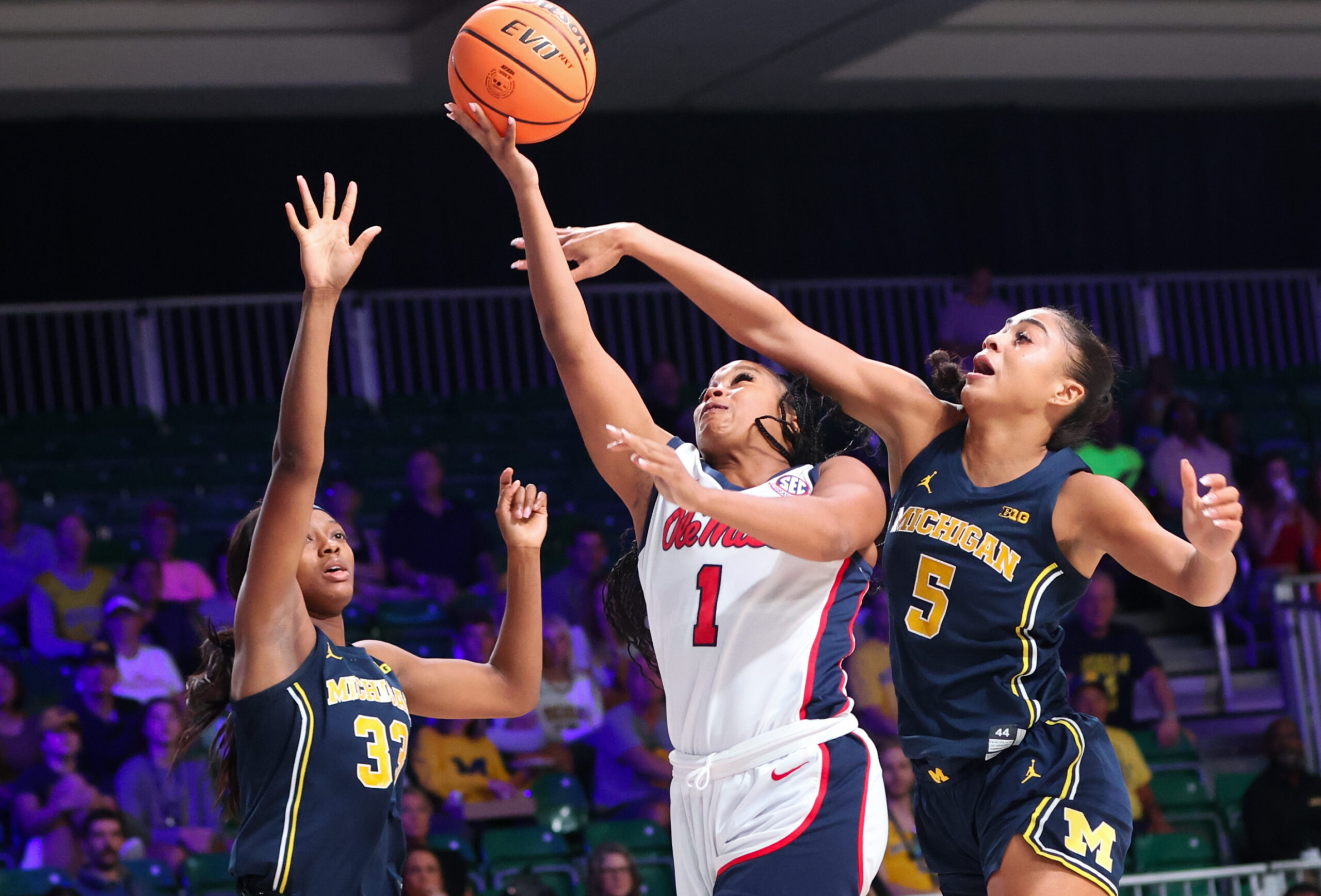 A woman shoots the basketball as two others try to defend her