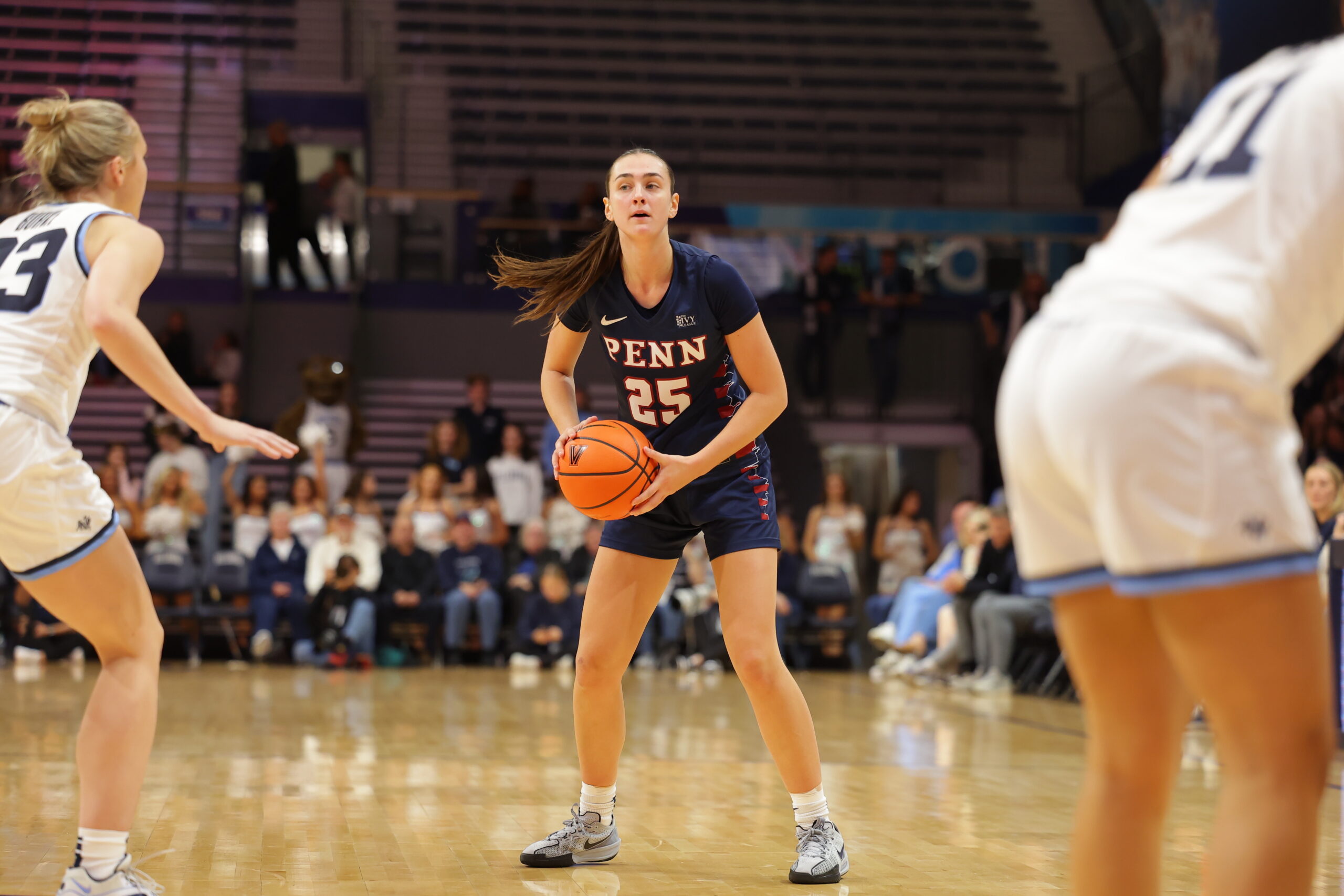 Penn forward Katie Collins holds the ball with two hands at about hip height as she stands on the perimeter and scans the court.