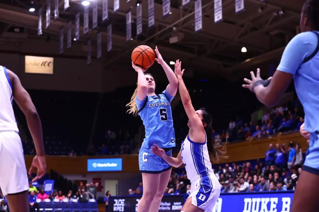 Columbia guard Mia Broom shoots a right-handed jump shot. Duke guard Vanessa de Jesus makes contact with Broom's left arm and midsection as she contests the shot.
