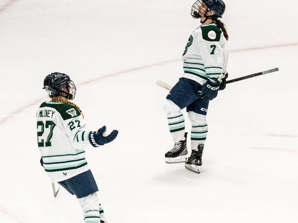 Morin pumps her fists and yells in celebration. Maloney is skating in for a hug. They are both wearing white away uniforms.