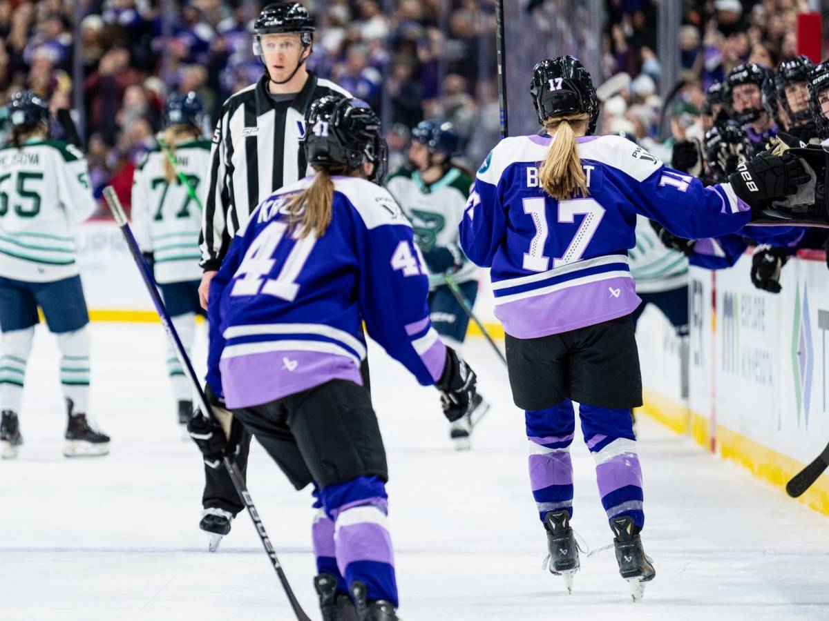 Bryant and Křížová skate down the handshake line at the bench, backs to the camera. They are wearing purple home uniforms.