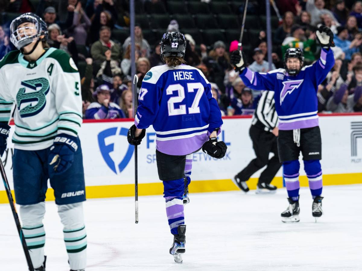 A from-behind picture of Heise lifting her leg and pumping her fists in celebration. She is wearing a purple uniform.