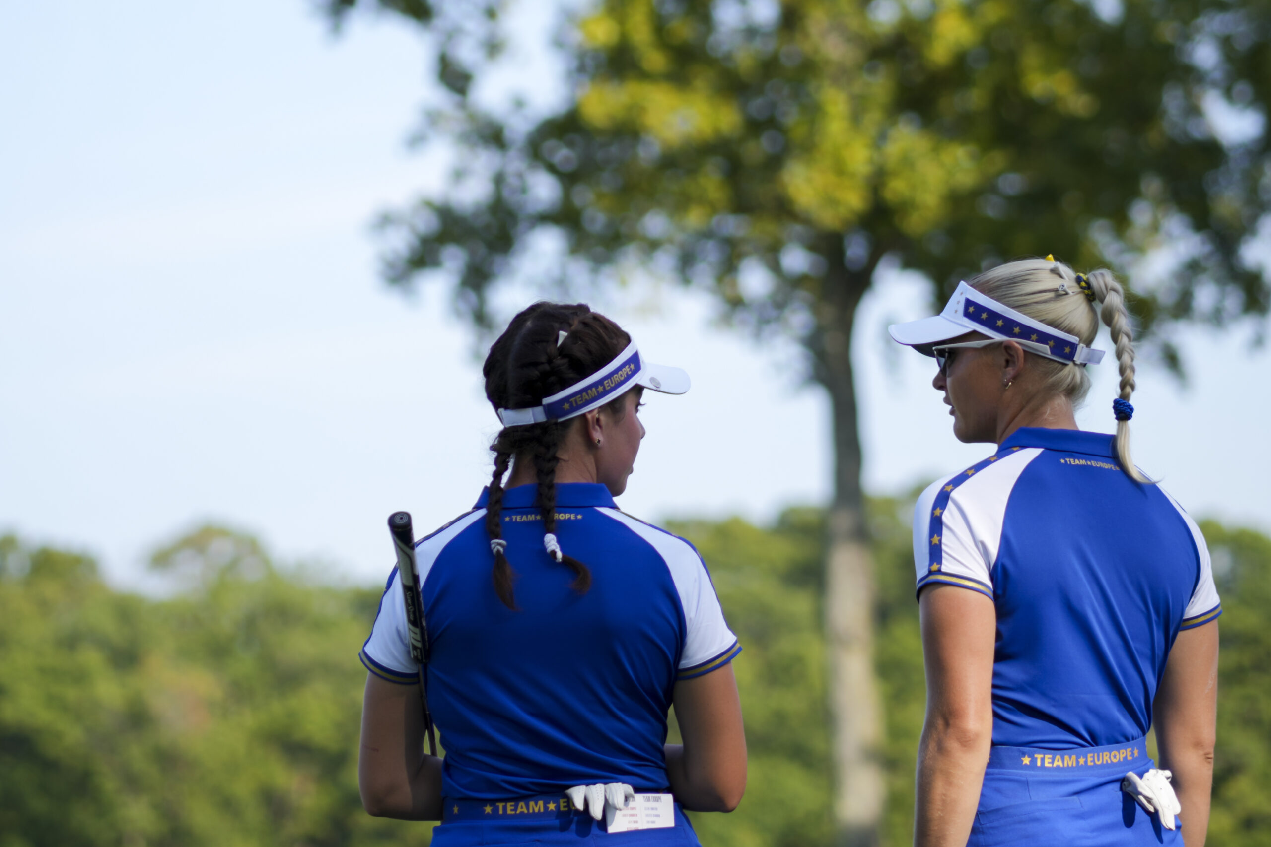 Charley Hull stands to the right of Georgia Hall. Their backs face the camera as they discuss a shot during the Solheim Cup.