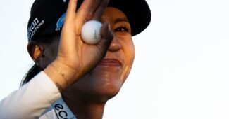 Lydia Ko smiles to the crowd, her hand holding the golf ball and raised in a wave that covers part of her face.