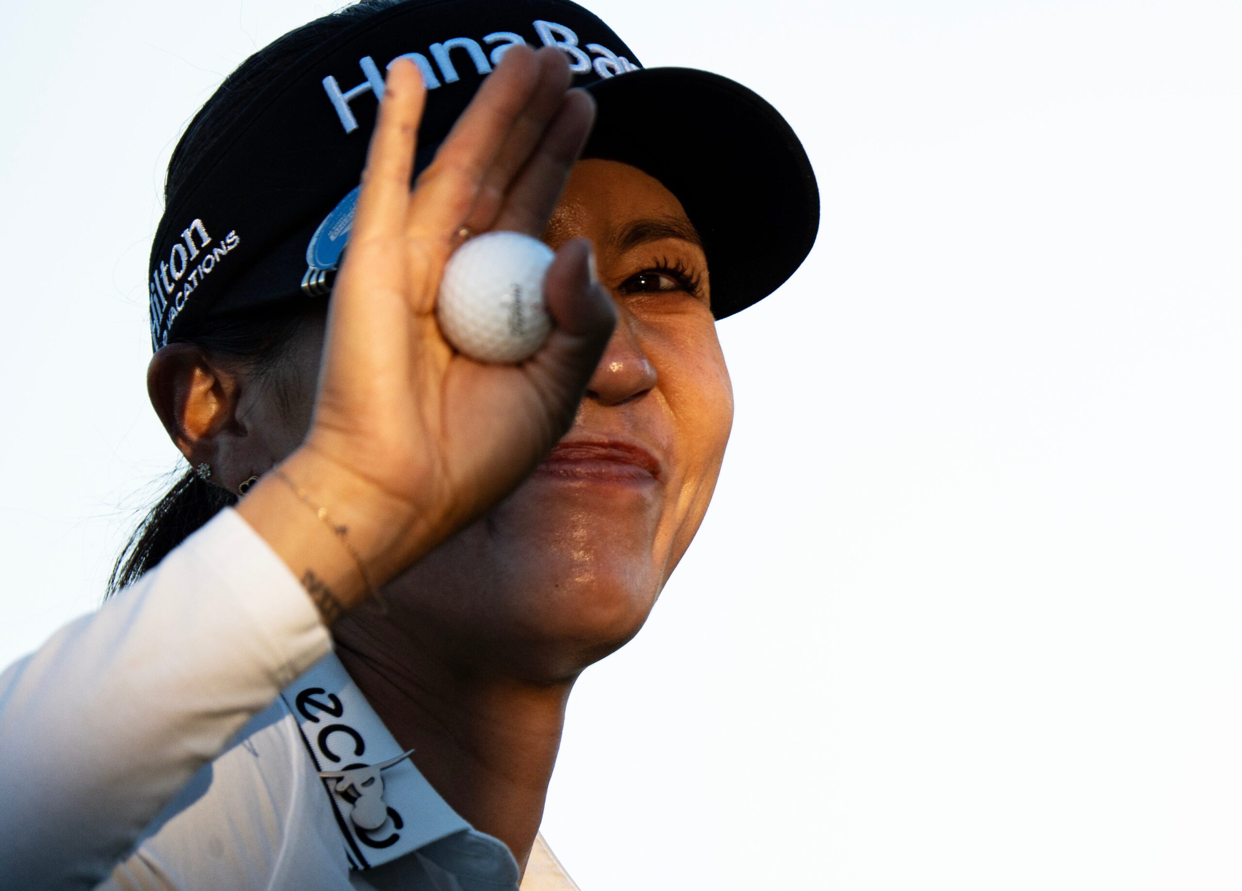 Lydia Ko smiles to the crowd, her hand holding the golf ball and raised in a wave that covers part of her face.
