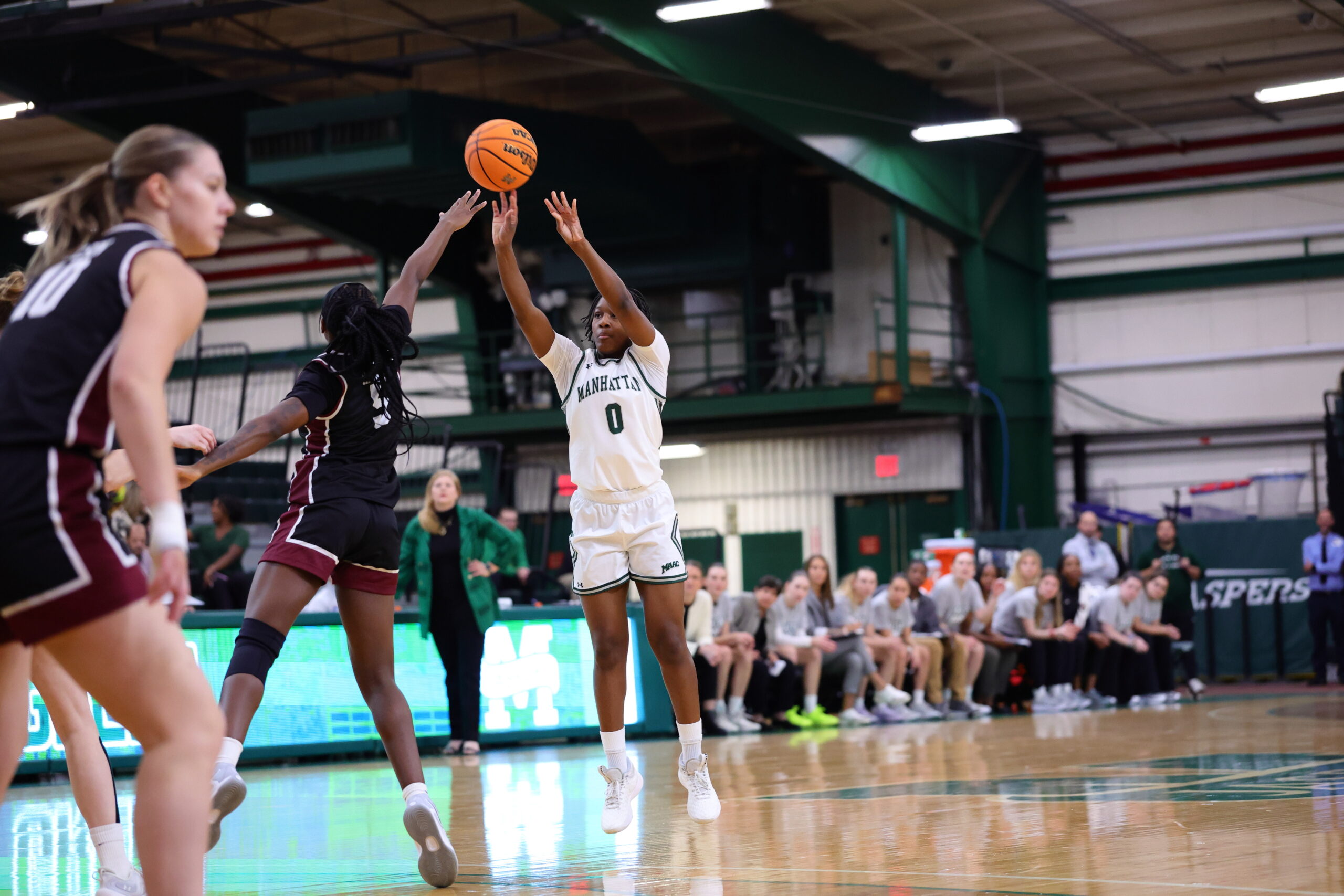 Manhattan junior guard Brianna Davis (in white) releases a jump shot with her right hand and looks toward the basket over Fordham junior guard Chae Harris (in black) in the Jaspers 65-58 win on Nov. 20. (Photo credit: Vincent Dusovic).
