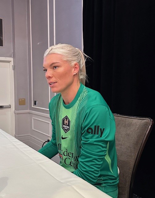 A woman sits at a table in a green goalkeeper jersey