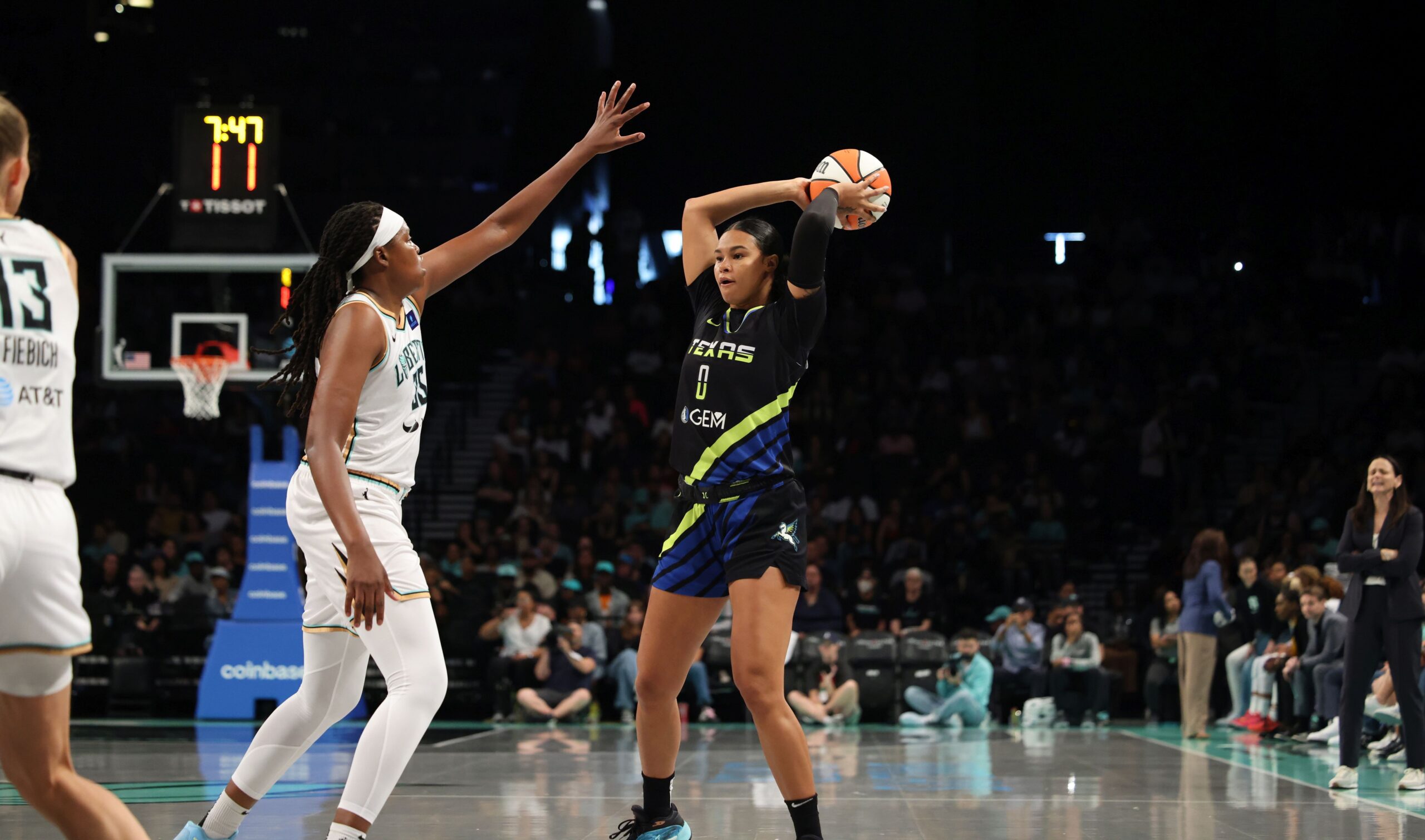 Dallas Wings forward Satou Sabally holds the ball over and behind her head to shield it from pressure by New York Liberty center Jonquel Jones while looking to pass as a packed WNBA crowd looks on behind them