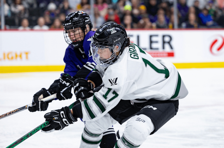 Girard (in white) reaches into a battle for the puck. The Minnesota player (in purple) is behind her to her right.