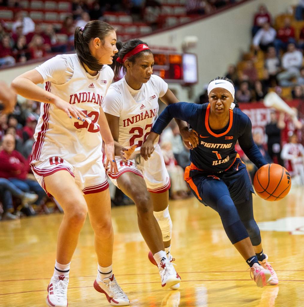 Illinois' Genesis Bryant drives past Indiana's Chloe Moore-McNeil and Lilly Meister while dribbling with her left hand.