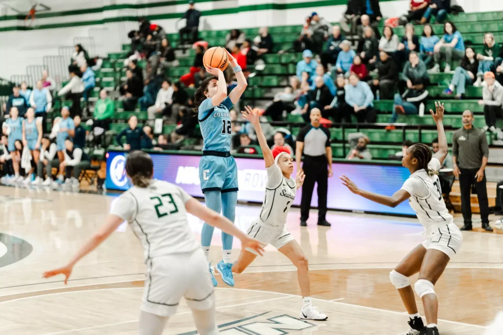 Columbia guard Marija Avlijas shoots a right-handed jump shot from near the free-throw line. None of the Wagner defenders in the frame are able to contest it.